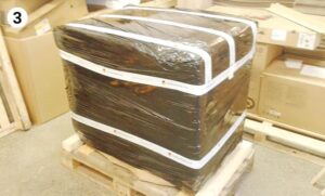 black plastic-wrapped package fastened with white straps on wooden pallet